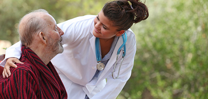 nurse leaning down speaking to seated resident