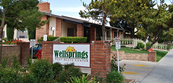 Wellsprings entrance sign with parking and lush trees out front