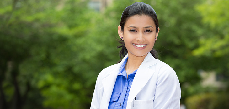 A doctor standing outside with lush bushes in the background