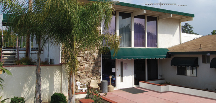 Entrance of the facility with a palm tree out front and canopies for shade above the entrance.