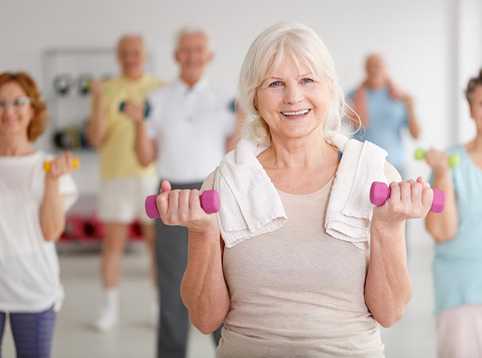 woman in group exercise class with small hand weights and a towel around her neck