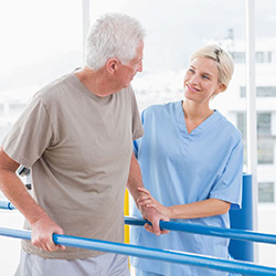 man using parallel walking bars for physical therapy with a therapist