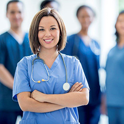 Smiling female nurse with shoulder length brown hair, crossed arms and a stethoscope.