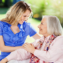 blonde woman in a blue shirt smiling at elderly woman with silver hair and a pink blouse