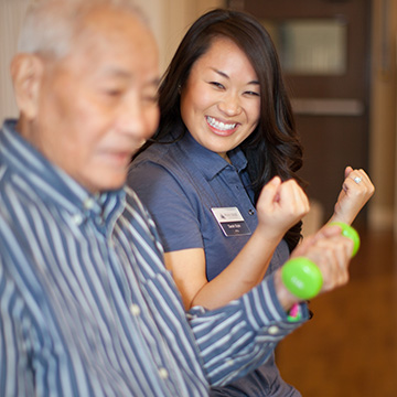 smiling therapist helping resident with weights